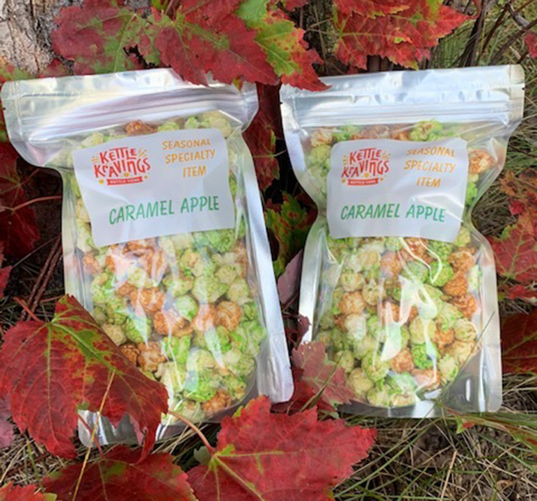 Two bags of caramel apple kettle corn laying in grass and leaves